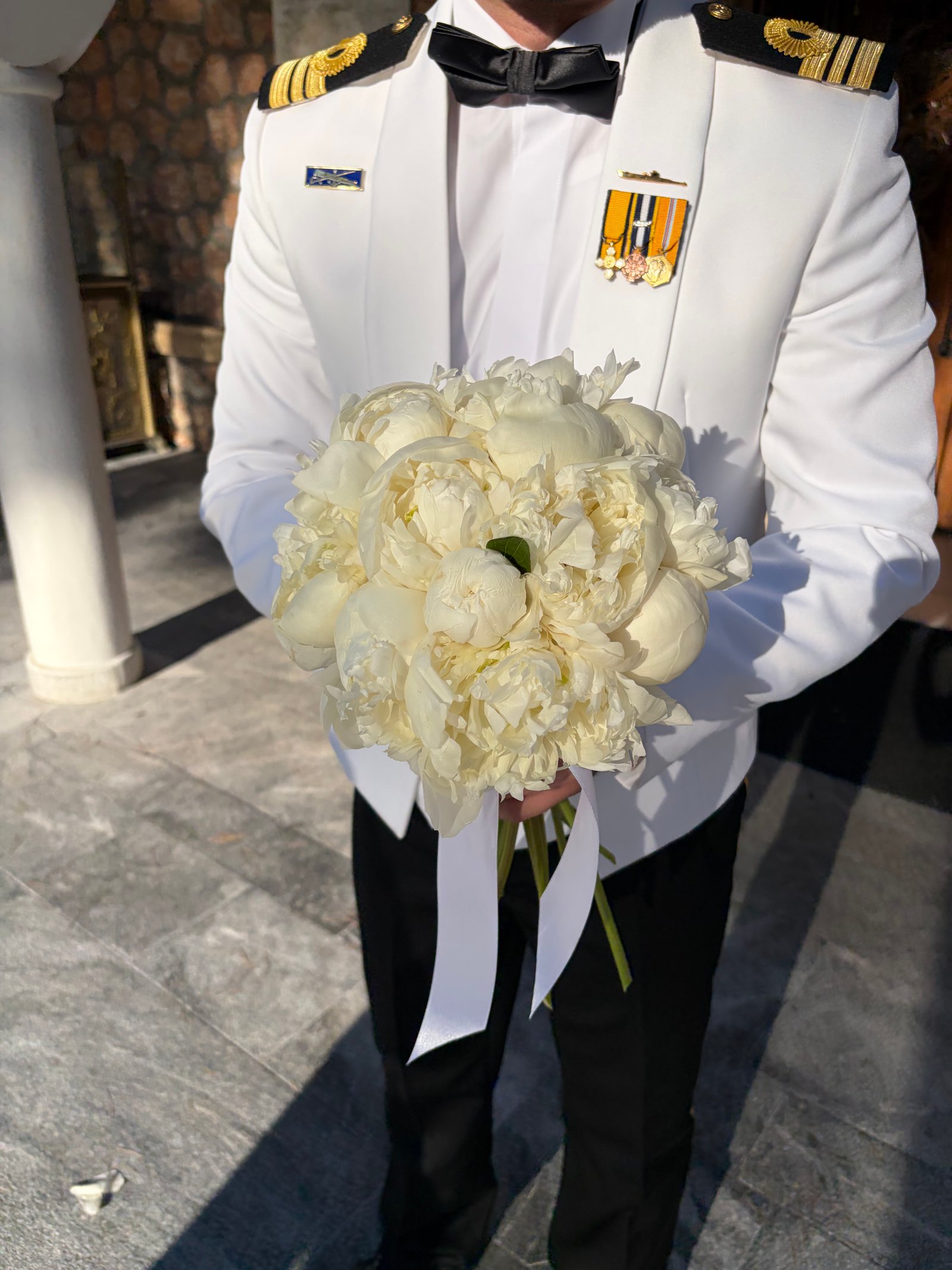 Groom in a white suit holding a bouquet of white peonies